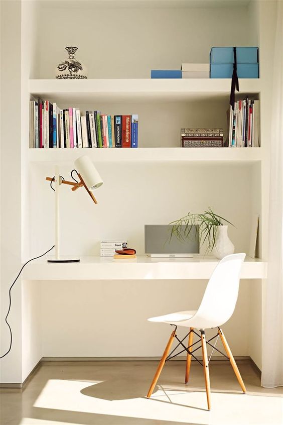 modern niche with shelves and a desk, books, a table lamp, some greenery and boxes for storage, a white chair