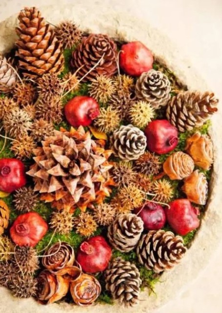 a bold rustic fall centerpiece of a bowl filled with moss, pinecones and pomegranates looks bold and fall-like