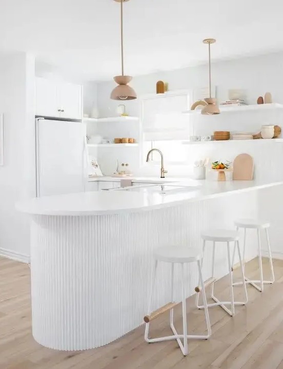 an all-white kitchen with sleek plain cabinets, a curved ribbed kitchen island that is an accent here, open shelving instead of upper cabinets