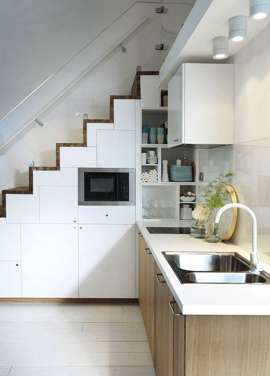 a Scandinavian kitchen with lower timber cabinets, a staircase consiting of white storage compartments, a shiny tile backsplash and spotlights