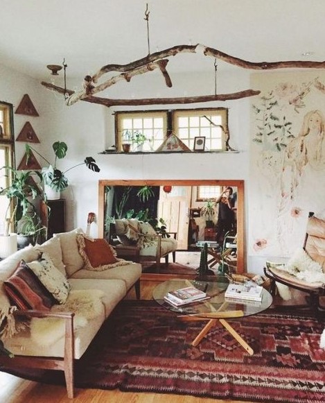 a boho space with boho rugs and pillows, branch hangings, a mirror, a glass coffee table and potted plants