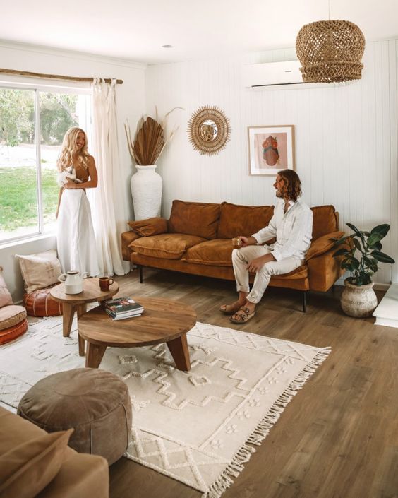 a booh living room with a rust-colored sofa, coffee tables, poufs and pillows, some dried leaves