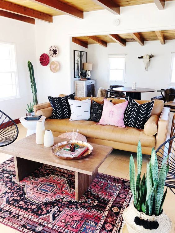 a bright and catchy boho living room with an amber sofa and printed pillows, a coffee table and a boho rug and potted plants