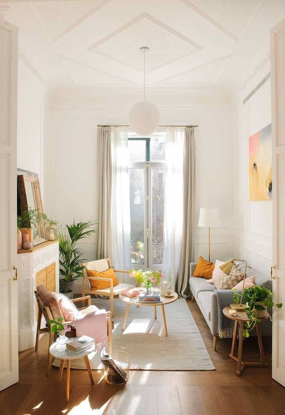 a bright boho living room with a grey sofa and bright pillows, a fireplace with a screen, chairs and som artworks