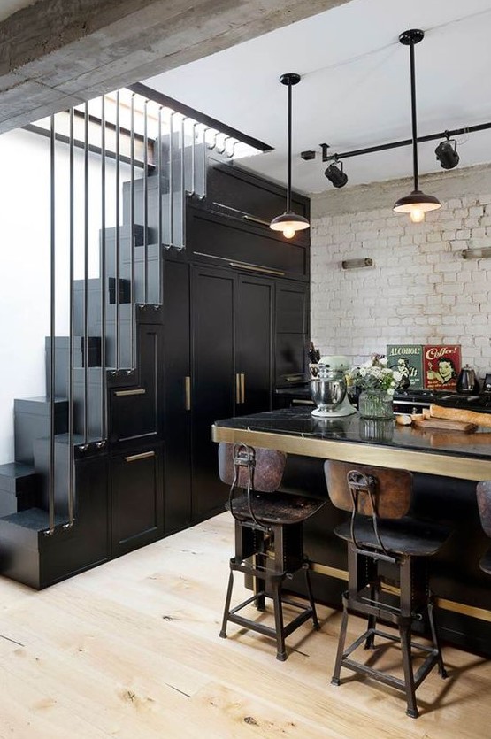 a catchy vintage kitchen in black with cabinetry built into the staircase, a large table that is a kitchen island and vintage decor