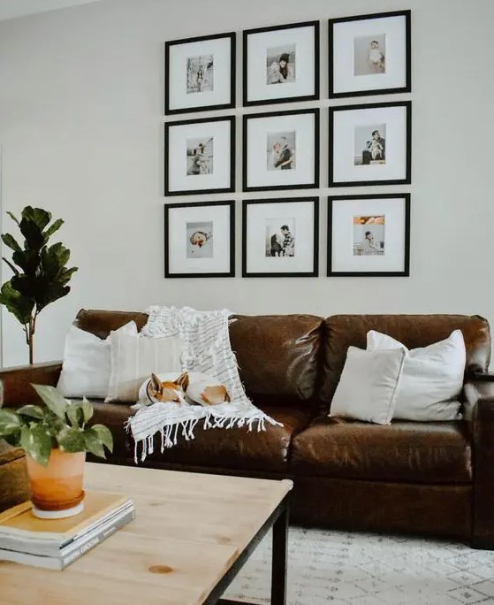 a cool boho living room with a brown leather sofa, a wooden coffee table, a grid gallery wall and potted greenery