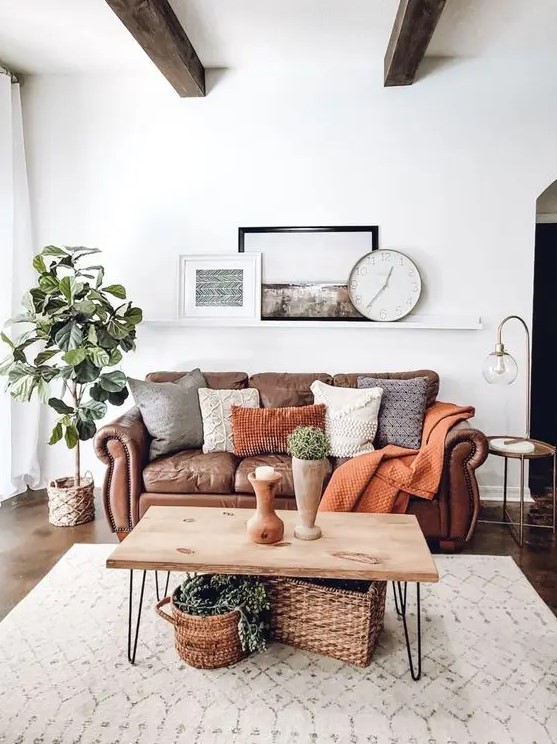 a cozy boho living room with a brown leather sofa and lots of pillows, a hairpin leg coffee table and baskets, a potted tree