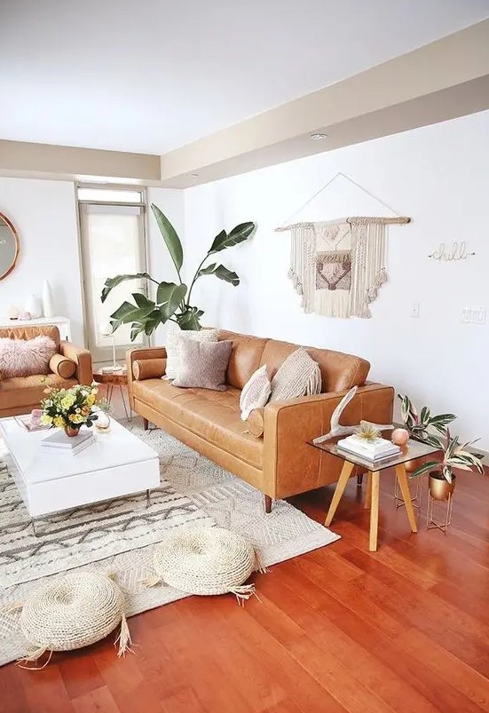 a mid-century modern to boho living room with tan leather furniture, a low white coffee table, woven poufs, a macrame hanging and potted plants