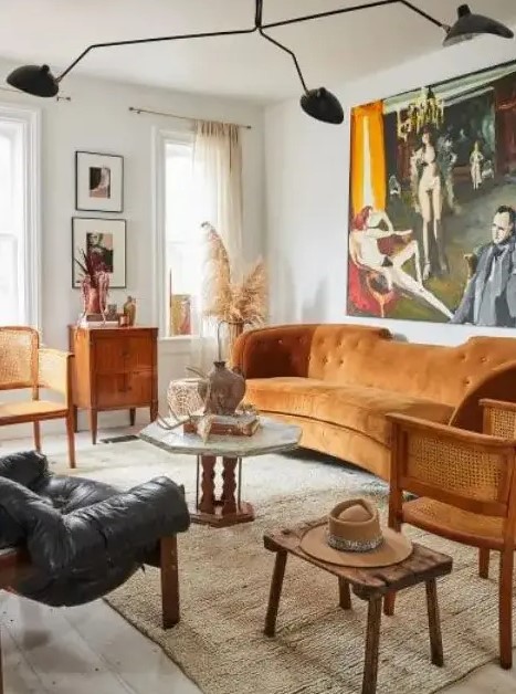 a modern and boho living room with a rust-colored sofa, rattan chairs, wooden and leather furniture and a statement artwork