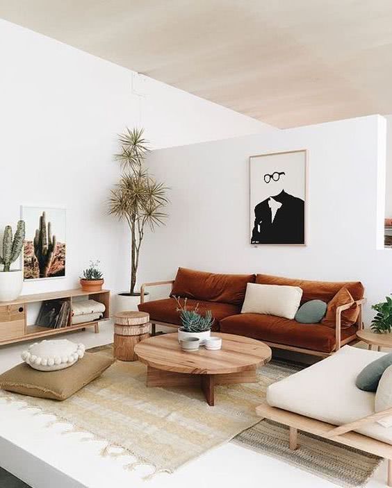 a modern boho living room with a burnt orange sofa and a neutral chair, a coffee table, a credenza, some art and plants