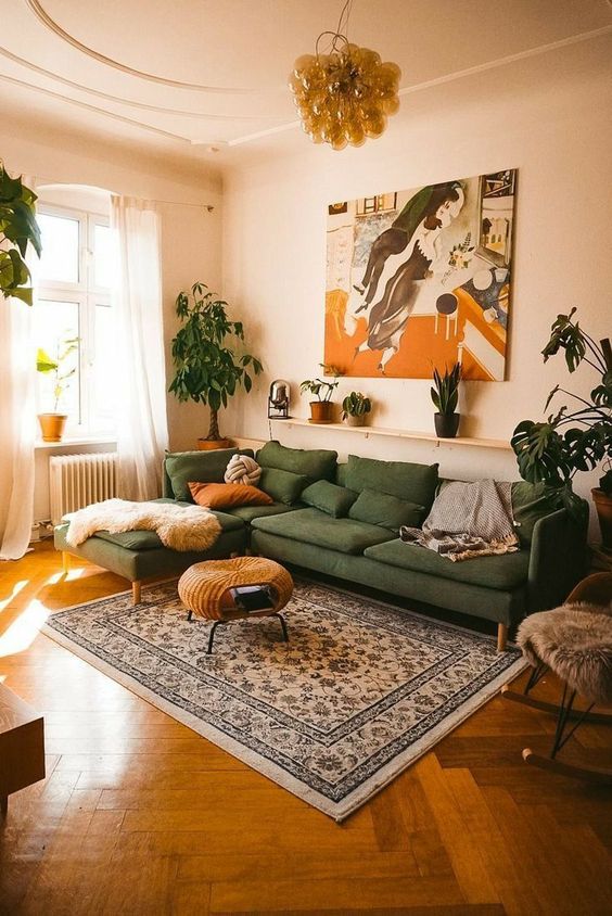 a modern boho living room with a green sofa with pillows, a woven coffee table, a bold artwork, a printed rug and some potted plants