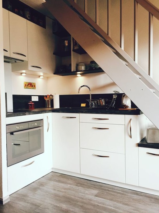 a modern kitchen placed partly under the staircase, with built-in lights, black countertops is a smart and cool idea