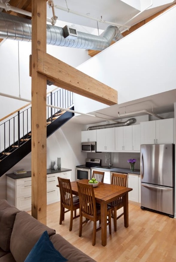 a modern kitchen with white cabinets and black countertops placed under the stairs, with a dining set of stained wood