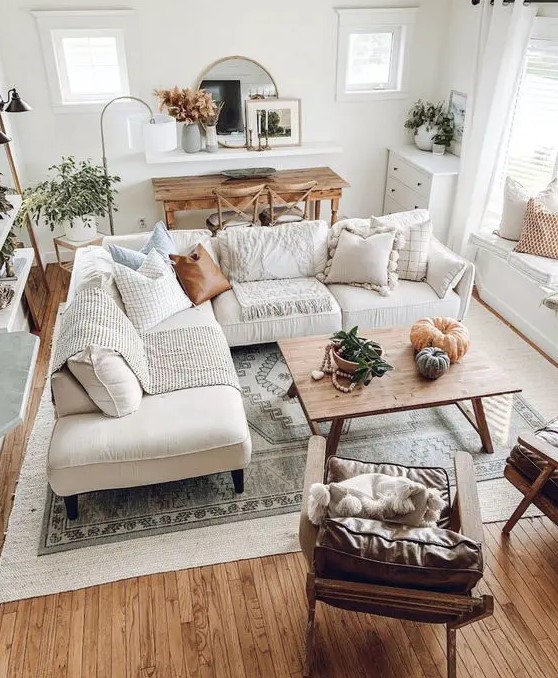 a neutral boho farmhouse living room with a white corner sofa, a wooden table, leather chairs, potted greenery and pumpkins