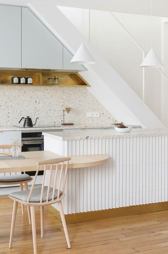 a refined contemporary kitchen with pale blue cabinets right under the stairs, a terrazzo countertop, a fluted kitchen island and pendant lamps