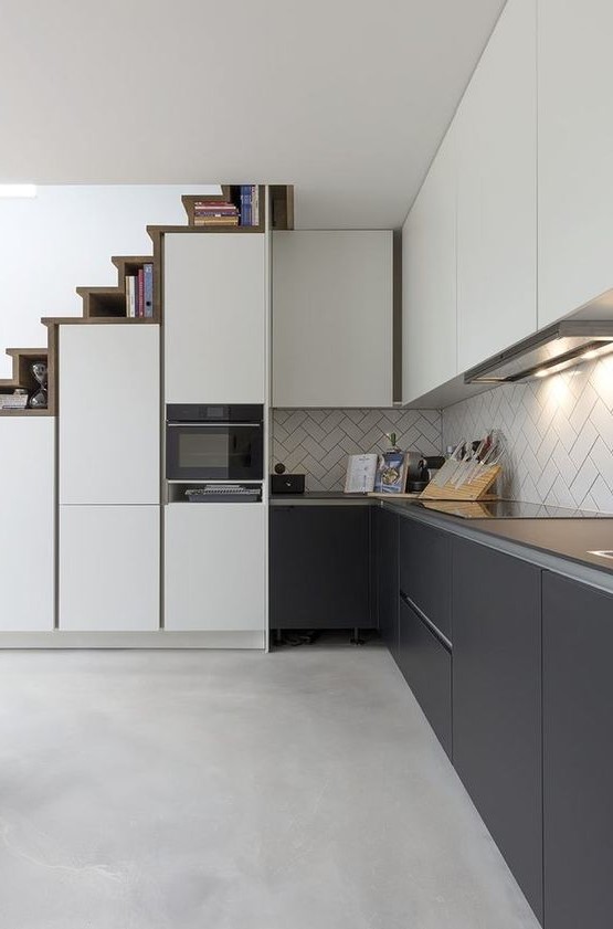 a sleek modern kitchen with upper white and lower soot cabinets, a herringbone backsplash, a staircase that hides storage compartments