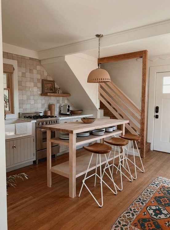 a small boho kitchen under the stairs, with grey lower cabinets, a stained kitchen island, tall stools, open shelves and pendant lamps