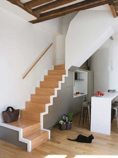 a small modern kitchen with grey cabinets built under the stairs, a kitchen island, pendant lamps and tall stools