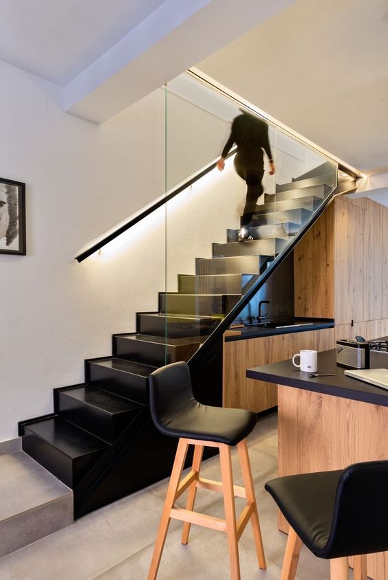 a stained kitchen built in under the staircase, with black countertops and lights, a matching kitchen island with black stools