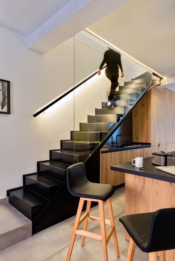 a super stylish modern kitchen placed under the stairs, with a black countertop and backsplash, a kitchen island with a black countertop