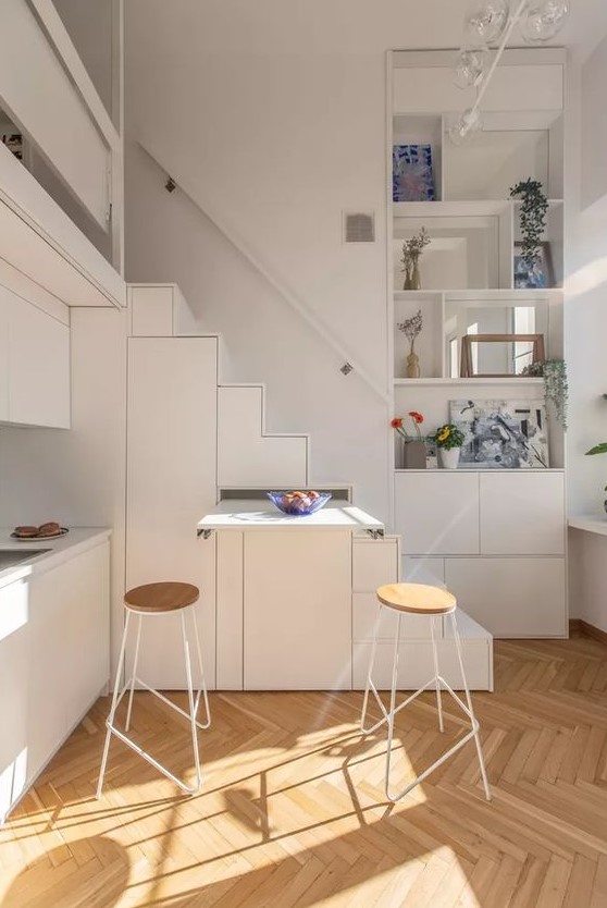 a tiny white kitchen partly built into the staircase, with a retracting table is a smart solution if you face lace of space