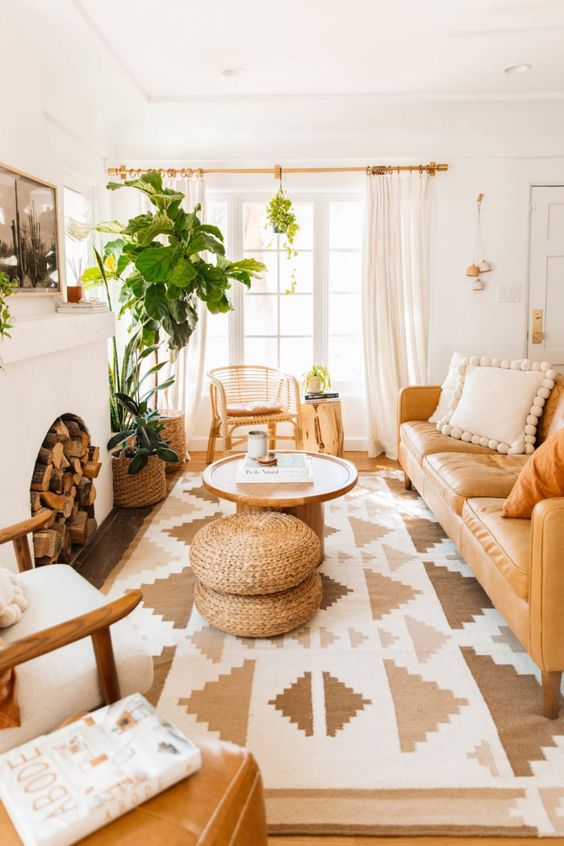 a welcoming boho living room with a fireplace with firewood, an amber leather sofa, neutral chairs, a coffee table and jute poufs