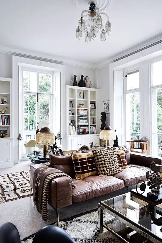 an amazing boho living room done in white, with bookcases and decor, made cozier with a brown leather sofa and a glass coffee table