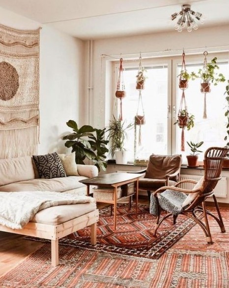 an elegant boho living room with rattan and wood furniture, boho rugs and pillows, planters in macrame hangers and a macrame hanging on the wall