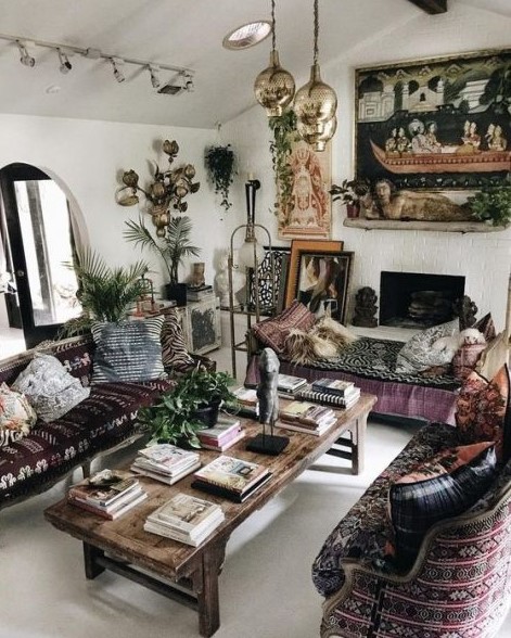 an epic gypsy living room with dark embroidered furniture, pendant lamps, a fireplace and boho pillows and artworks