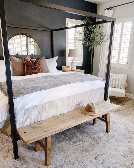 34 A Modern Farmhouse Bedroom With A Black Accent Wall A Black Canopy Bed A Stained Bench A Potted Tree And A Creamy Chair 