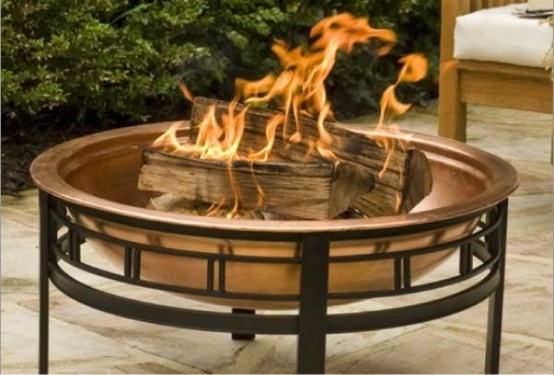 a large and beautiful copper fire bowl on a comfortable black metal stand is a lovely solution for many backyards, it will add a soft touch of color to the space