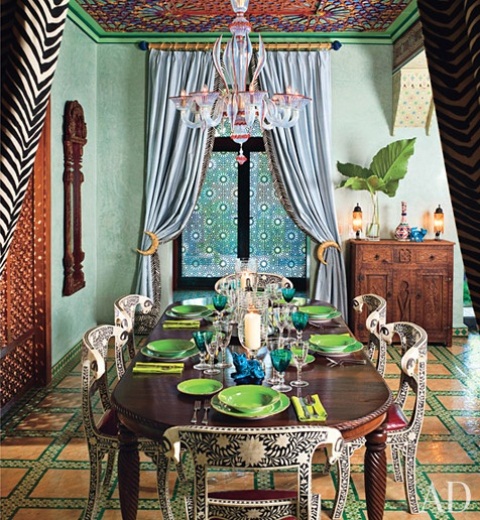 غرفة طعام مشرقة مستوحاة من الطراز المغربي مع أرضية زاهية محددة ، وسقف عريض ، وطاولة ثقيلة منحوتة وكراسي مطلية بالإضافة إلى منسوجات مطبوعة جريئة