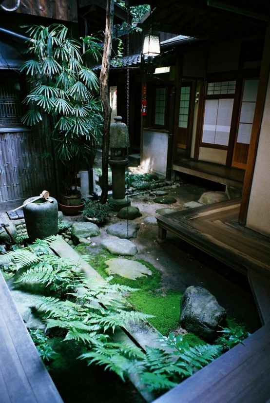 un patio trasero japonés con musgo, helechos, rocas, faroles de piedra y un árbol bajo para un espacio tranquilo y acogedor