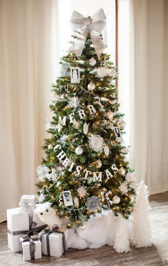 شجرة عيد الميلاد متطورة بأضواء ، مع زخارف بيضاء وذهبية ، وصور ، وأزرار وأكليل من الورق بالإضافة إلى قوس فضي في الأعلى